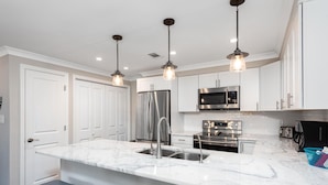 Una cocina moderna con armarios blancos, electrodomésticos de acero inoxidable, encimera de mármol e iluminación colgante.