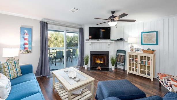 Una sala de estar con chimenea, sofás azules, un televisor y un ventilador de techo.