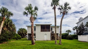 A two-story house with a front porch, surrounded by a well-maintained lawn and palm trees.