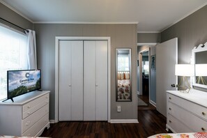 A room with a closed door, a television on a dresser, and a bed with a view of another room.