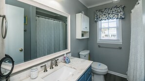 A bathroom with a large mirror, a sink, a toilet, and a window with blinds.
