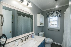 Een badkamer met een grote spiegel, een wastafel, toilet en een raam met zonwering.