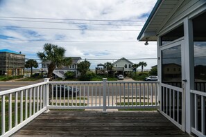 A wooden deck with a white railing, overlooking a street with parked cars and houses.