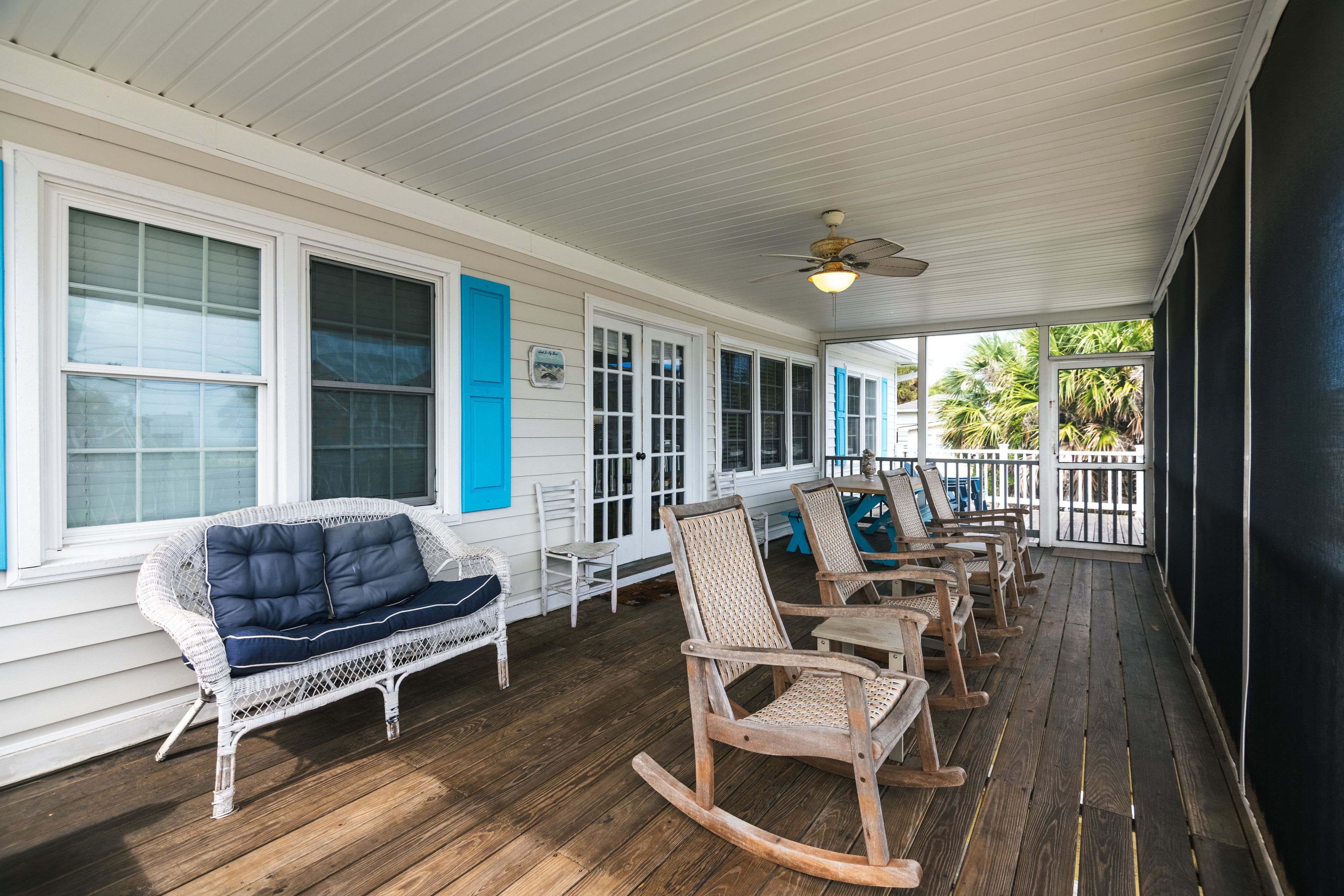 A covered porch with white wooden railings, a ceiling fan, and a row of wooden rocking chairs.