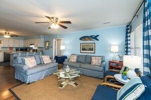 A living room with a ceiling fan, a dining area with a kitchen, and a view of the ocean through a window.