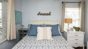 A bedroom with a bed, a bedside table, a lamp, and a wall with a 'beach' sign.