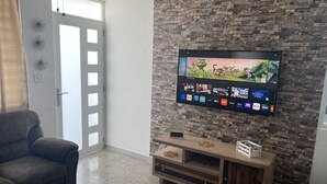 A living room with a TV mounted on a brick wall, a gray sofa, and a wooden entertainment unit. - Lucor D- Eight House (Rincon PR)