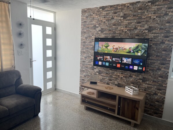 Una sala de estar con un televisor montado en una pared de ladrillo, un sofá gris y un mueble de madera para el equipo electrónico.