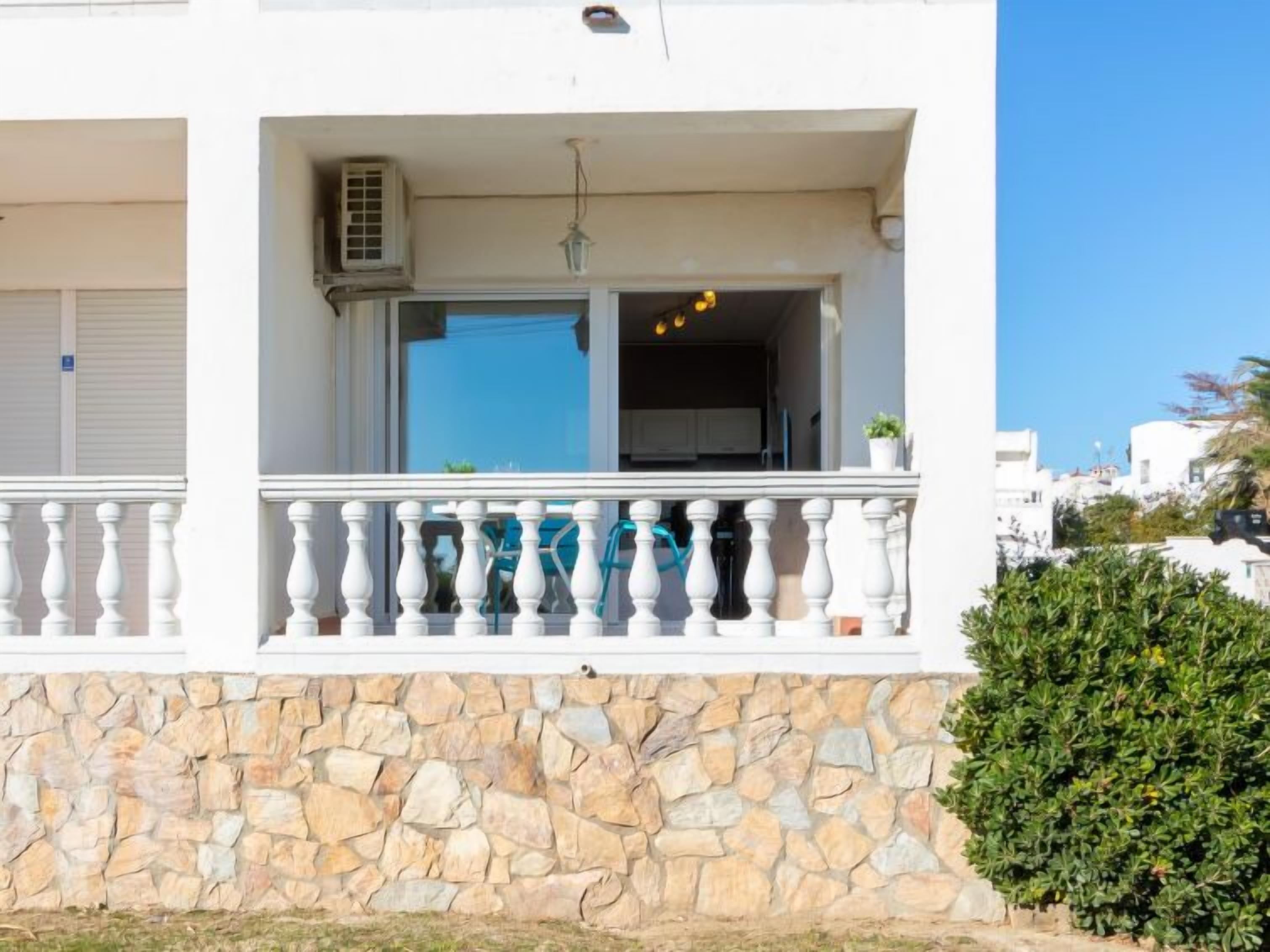 Un bâtiment doté d’une façade en pierre, d’un balcon avec des balustrades blanches, et d’un ciel bleu clair en arrière-plan.