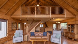 Un vaste espace de vie doté d’un haut plafond, de poutres apparentes, d’un canapé central en cuir, de deux fauteuils, d’une table basse en bois et d’un escalier menant à un niveau supérieur.