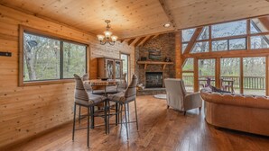 L’intérieur d’un chalet en bois comprend un coin repas, une cheminée et de grandes fenêtres.