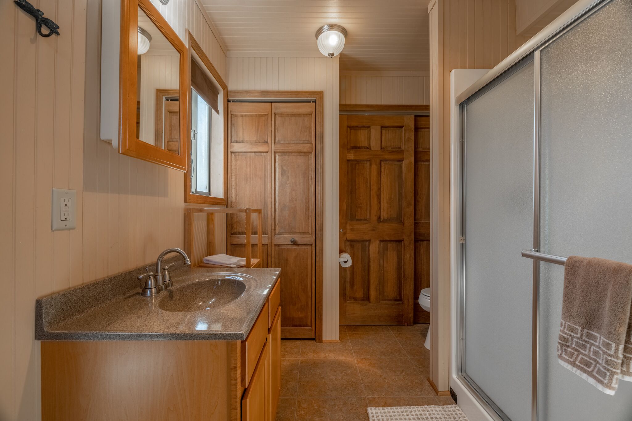 Un bagno con un lavandino in granito, armadietti in legno, uno specchio e una doccia con un asciugamano appeso alla porta.