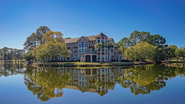 A large, multi-story building with a symmetrical facade, a central entrance, and a reflection in the calm water in front. - Fisherman's Cove- Golf cart included (Miramar Beach)