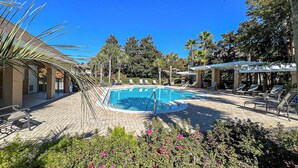 A swimming pool surrounded by lounge chairs and covered seating areas, with palm trees and a clear blue sky in the background. - Fisherman's Cove- Golf cart included (Miramar Beach)