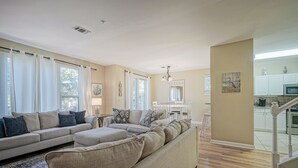A spacious living room with a large sectional sofa, a dining area with a white table and chairs, and a kitchen area with white cabinets and a microwave. - Fisherman's Cove- Golf cart included (Miramar Beach)