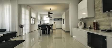 A modern kitchen with a dining area, a black sofa, and a TV mounted on the wall.