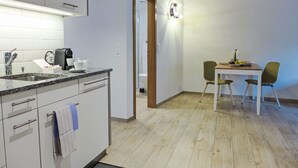 Une cuisine moderne équipée d’un four encastré, d’une machine à café et d’un évier. On y trouve également un coin repas avec une table et deux chaises.