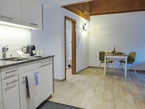 A modern kitchen with a built-in oven, a coffee machine, and a sink. There is a dining area with a table and two chairs. - Schwendi 3 by Interhome (Grindelwald)