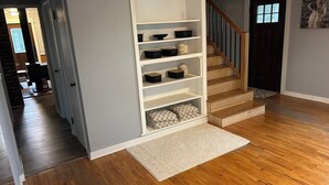 A hallway with a white shelving unit, wooden flooring, and a staircase.