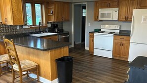 A kitchen with wooden cabinets, a granite countertop, a stove, a microwave, and a refrigerator.