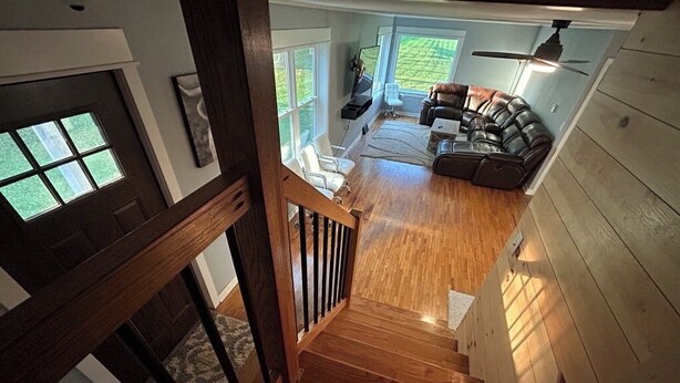 A wooden staircase leading to a living area with a leather sofa, a television, and a view of the outdoors.