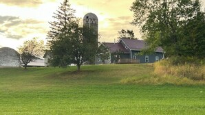 A rural landscape with a barn, a silo, and a house with a red roof.