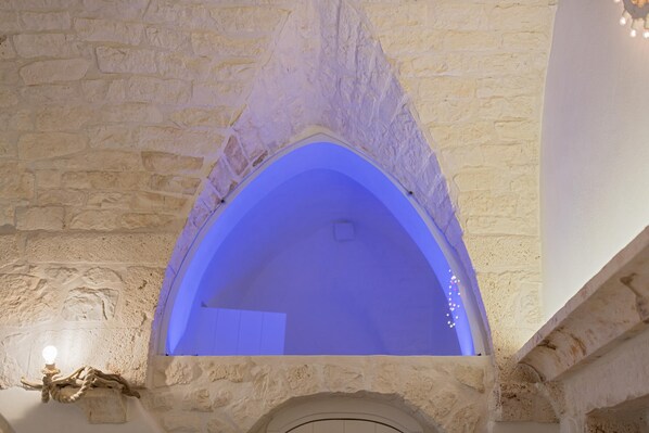 A stone archway with a blue-lit interior, a rustic wooden sculpture, and a white door.