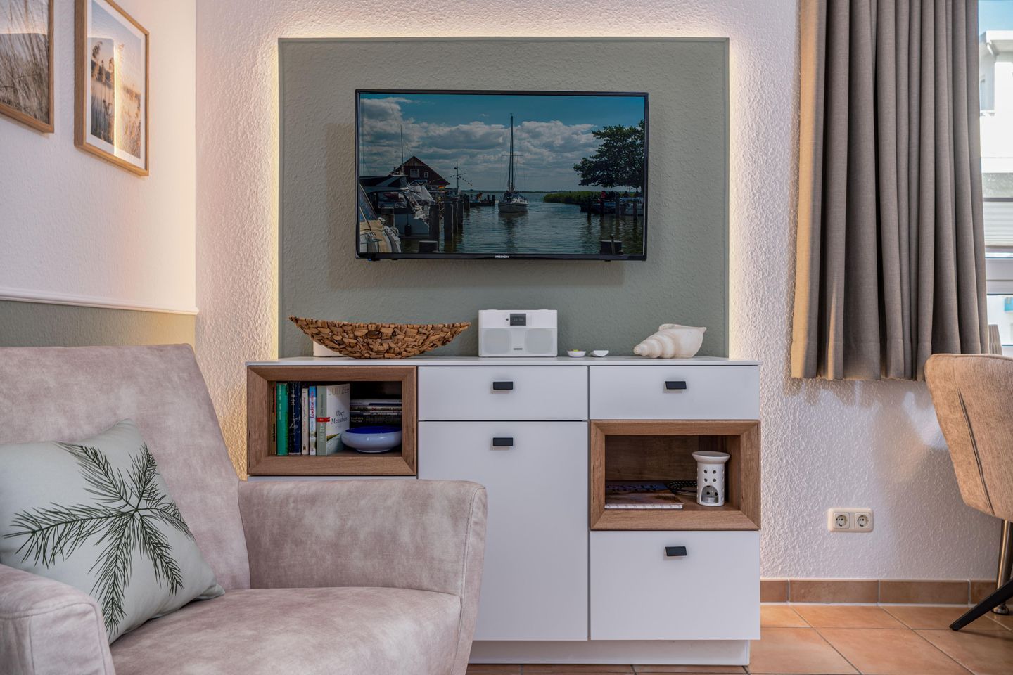 A living room with a sofa, a coffee table, a TV mounted on the wall, and a small cabinet with decorative items.