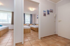 Ein Hotelzimmer mit Bett, Schreibtisch und Stuhl. Ein Fenster mit Vorhängen und ein fest an der Wand befestigtes Telefon sind ebenfalls vorhanden.