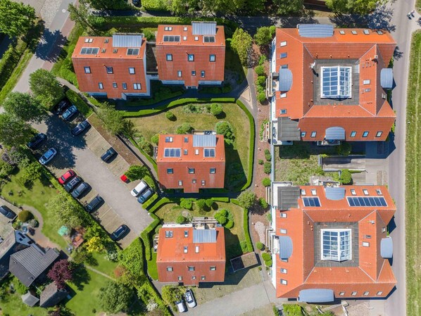 Un ensemble résidentiel composé de plusieurs bâtiments aux toits rouges, dotés de panneaux solaires et comprenant un espace de stationnement.