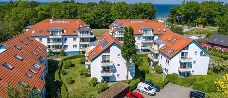 A residential complex with multiple apartment buildings, a parking area, and a view of the sea.