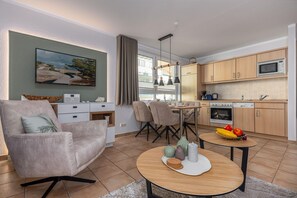 Ein modernes Wohnzimmer mit einer Couch, einem Esstisch und einer Küchenzeile mit Holdekorfronten und Geräten.