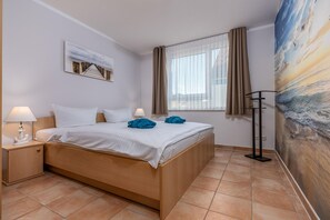 A hotel room with a bed, a nightstand, a lamp, a painting, a window with curtains, and a wall mural.