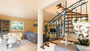 A modern living room with a dining area, a staircase with blue railings, and a view of the outdoors through large windows. - L'Italienne by Interhome (Saint Cyr sur mer Les Lecques)