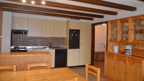 A kitchen with wooden cabinets, a black refrigerator, a tiled backsplash, and a wooden dining table with chairs. - Nice flat for rent in les Collons (Thyon-Les Collons)