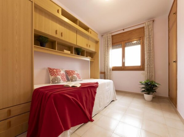 A bedroom with a bed, a red blanket, a potted plant, and wooden shelving.