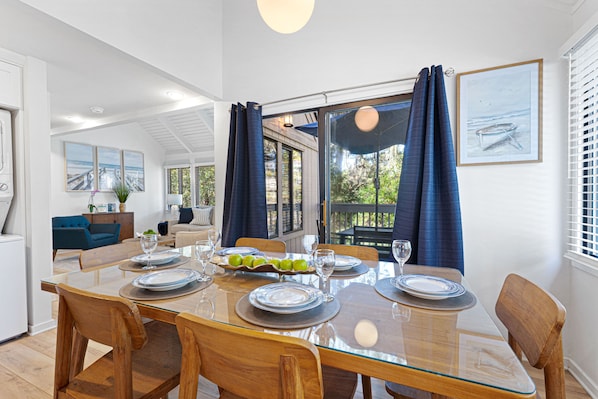 A dining area with a glass table, wooden chairs, and a view of the outdoors. - Sea Pines Cottage •Sleeps 10 •Close to Trails & Beach •Bike Everywhere (Hilton Head Island)