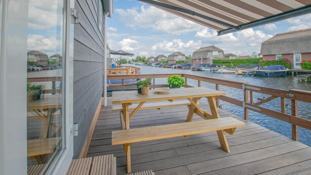 Eine Holzterrasse mit Picknicktischen mit Blick auf einen Kanal mit Booten und Häusern.