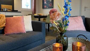 Ein modernes Wohnzimmer mit einem dunkelgrauen Sofa, einer Blumenvase und einem Tisch mit Kerzen.