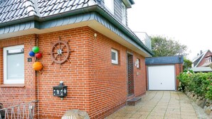 A brick house with a tiled roof, a garage, and a small garden area with a rock and a mailbox. - Calla - House Dünenblick - Calla (Sylt)