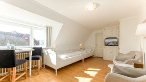 A bedroom with a bed, a desk with chairs, a TV, and a window with curtains. - Calla - House Dünenblick - Calla (Sylt)