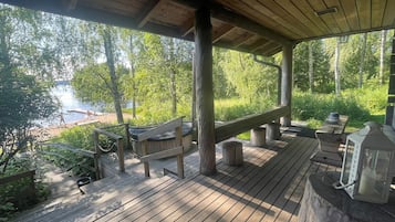 Una terraza de madera con un jacuzzi, barandas de madera y vista a un lago.