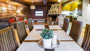A cozy cabin interior with a dining area, wooden walls, a fireplace, and a kitchen in the background. - Metsäpirtti by Interhome (Virrat)