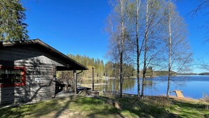 A cabin with a stone foundation and a red-framed window, situated by a lake with a dock extending into the water. - Metsäpirtti by Interhome (Virrat)