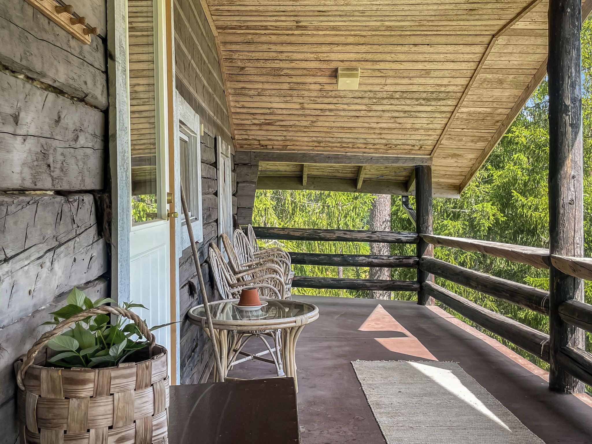 A wooden porch with wicker furniture, a potted plant, and a view of greenery.