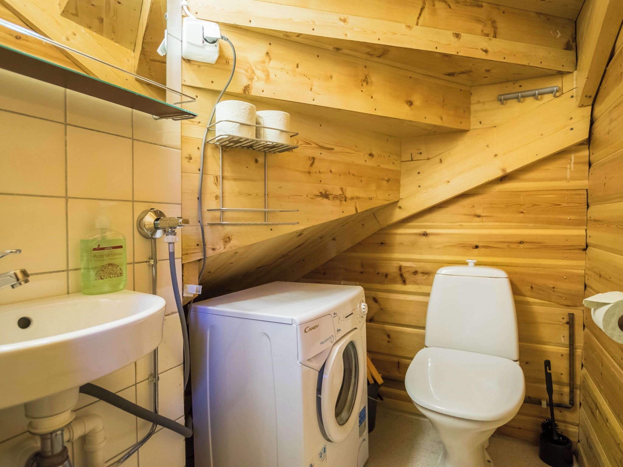 A compact wooden cabin bathroom with a sink, toilet, washing machine, and shower.