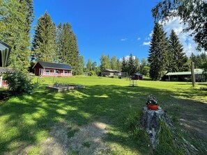 A red cabin with a fenced yard, surrounded by tall trees and a clear sky.