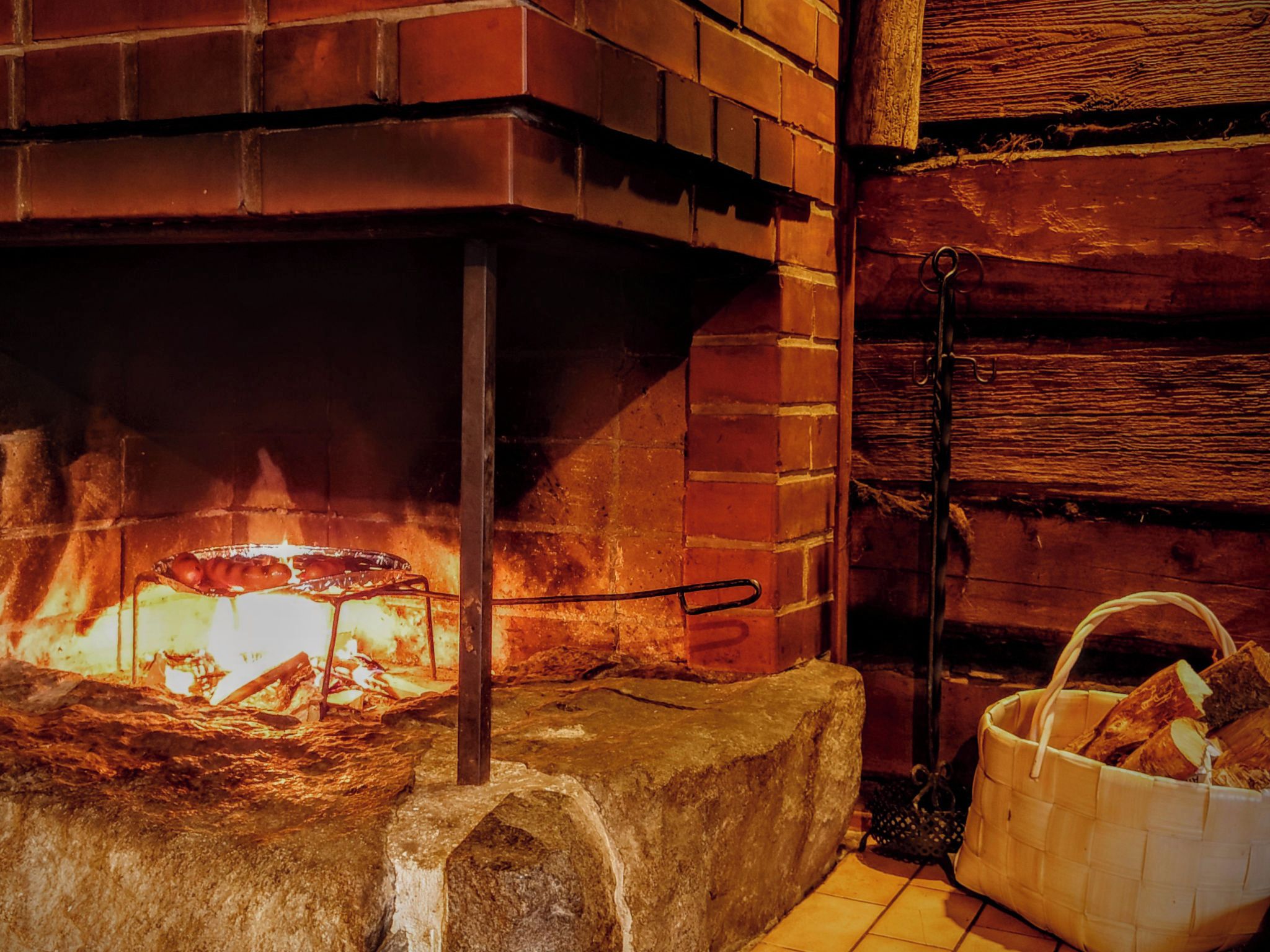 Una chimenea con leña, un portaobjetos metálico y una cesta de leña.