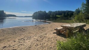 A sandy beach with a wooden dock extending into calm waters, surrounded by dense forest. - Metsäpirtti by Interhome (Virrat)