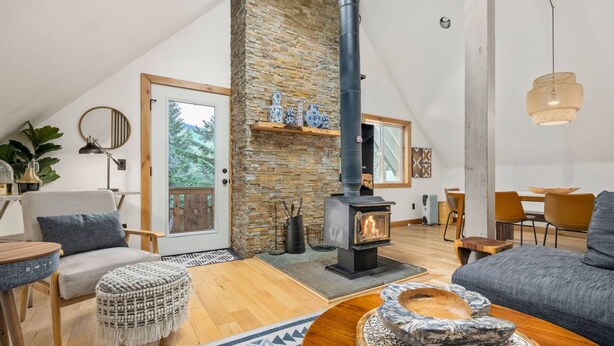 A cozy living room with a stone fireplace, wooden furniture, and a view of the outdoors through a door.